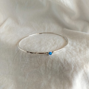 May include: A silver bangle bracelet with a hammered finish and a single blue opal gemstone.