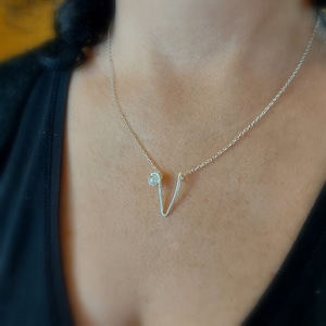 Può includere: Una collana d'argento con un delicato ciondolo a forma di V e un piccolo accento di perla.
