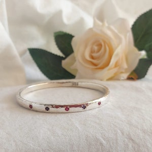 Pode incluir: Um bracelete de prata com textura martelada e cinco pequenas pedras preciosas cor-de-rosa engastadas na banda.