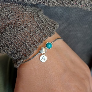 Può includere: Un braccialetto rigido in argento con una pietra turchese, un ciondolo a forma di cuore e un ciondolo con la lettera 'A'.