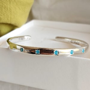 May include: A silver bangle bracelet with four turquoise gemstones set into the band.