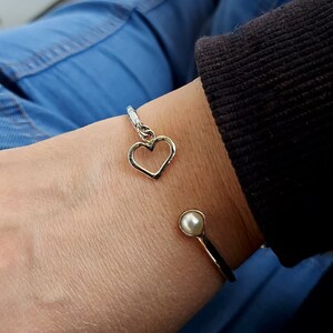 May include: A gold bangle bracelet with a heart charm and a pearl accent.