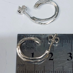 K&ouml;nnte beinhalten: Zwei silberfarbene Creolen. Jeder Ohrring hat einen Stecker und ein doppellagiges, C-f&ouml;rmiges Design. Die Ohrringe werden neben einem Lineal gezeigt, mit einem Durchmesser von etwa 1,9 cm.