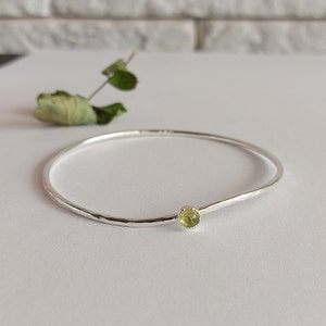 Pode incluir: Um bracelete de prata com acabamento martelado e uma única gema verde engastada no centro.