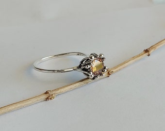 May include: A silver ring featuring a round, light brown gemstone set in a delicate, ornate design.