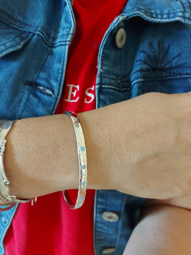 May include: A silver bangle bracelet with a hammered finish and small turquoise stones set into the metal.