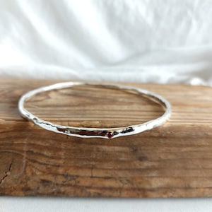 May include: A silver bangle bracelet with a hammered texture and a small red gemstone accent.