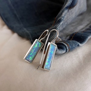 May include: A pair of silver dangle earrings with rectangular blue opal stones. The earrings have a simple design and are perfect for everyday wear.