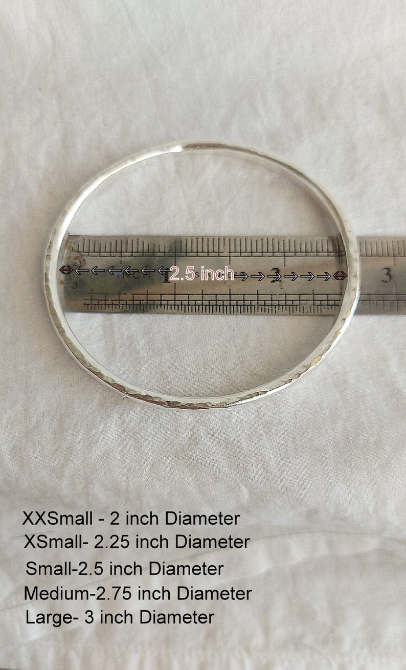 May include: A silver bangle bracelet with a hammered texture. The bracelet is measured against a ruler, showing a diameter of 2.5 inches. The image also includes text listing different sizes and their corresponding diameters: XXSmall - 2 inch Diameter, XSmall - 2.25 inch Diameter, Small - 2.5 inch Diameter, Medium - 2.75 inch Diameter, Large - 3 inch Diameter.