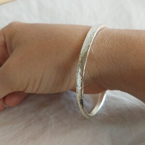 May include: A silver hammered bangle bracelet. The bracelet is thick and has a smooth, polished finish.