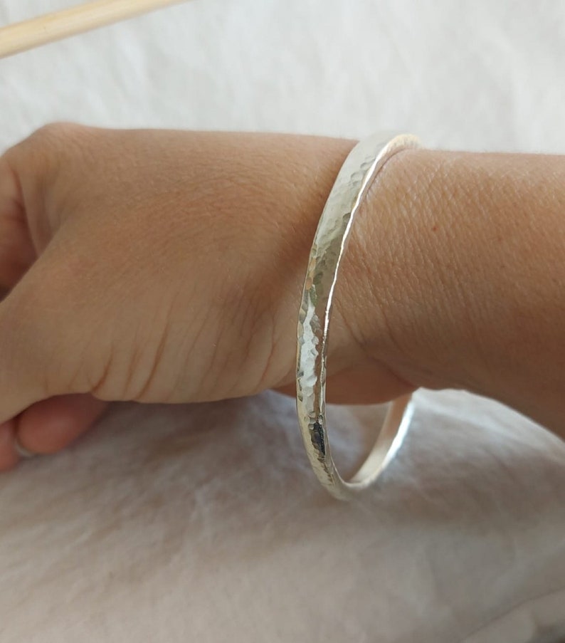May include: A silver hammered bangle bracelet. The bracelet is thick and has a smooth, polished finish.