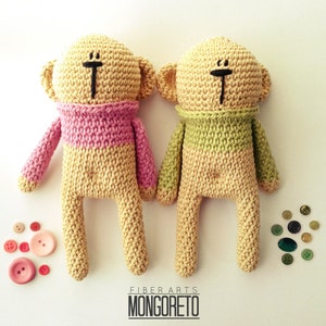 May include: Two crocheted teddy bears with pink and green sweaters. The bears have black eyes and a simple smile. The bears are standing on a white background with buttons scattered around them.