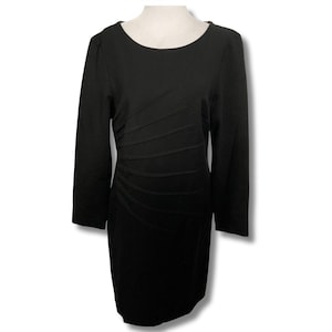 Puede incluir: Vestido negro de manga larga con cuello redondo. El vestido presenta una silueta entallada con detalles de pliegues horizontales en la parte delantera, creando una forma favorecedora. El vestido se muestra en un maniquí.