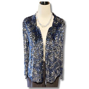 May include: A long-sleeved, open-front jacket with a blue and black floral pattern. The jacket is displayed on a mannequin with a white top and a gray skirt. A beaded necklace is also visible.