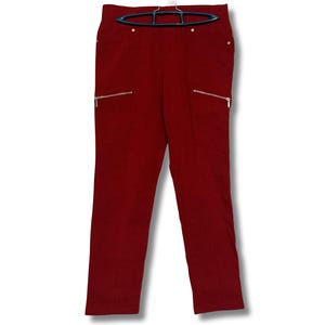 Può includere: Pantaloni color bordeaux con due tasche anteriori con cerniere dorate. I pantaloni sono appesi a una gruccia nera su sfondo bianco. I pantaloni hanno un design a gamba dritta.