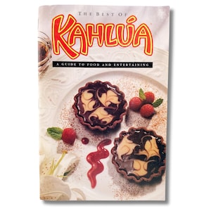 May include: A cookbook cover titled "The Best of Kahlúa" with a plate of desserts. Two chocolate tarts with cream filling are garnished with raspberries and mint. The cover also includes a glass of a dark liquid.