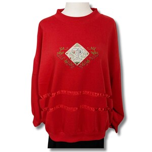 Pode incluir: Camisola vermelha com um design bordado em forma de diamante que apresenta uma letra "P" e detalhes florais.
