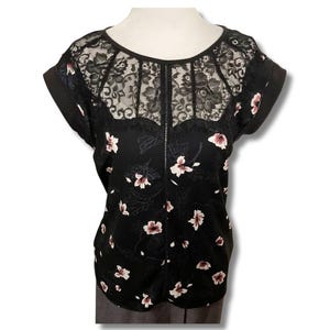 May include: Black floral print top with a lace yoke and short sleeves. The top features a scoop neckline and a pattern of white and burgundy flowers. The sleeves are cuffed with a solid black fabric.