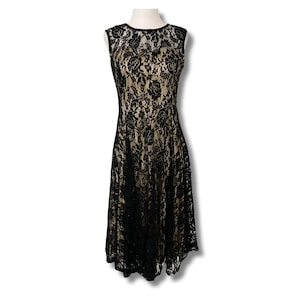 Pode incluir: Um vestido sem mangas de renda preta com decote redondo. O vestido tem um corpete justo e uma saia rodada, e é exibido em um manequim. A renda revela um forro bege.