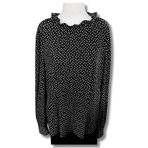 以下が含まれることがあります： 小さな形の白い繰り返し模様の黒い長袖トップス。 トップスはフリルネックラインと袖口が付いています。 衣類は白い背景に白いマネキンに展示されています。