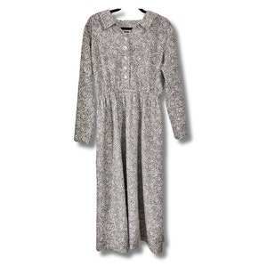 Puede incluir: Un vestido de manga larga con fondo blanco y estampado floral negro. El vestido tiene cuello y cierre de botones.