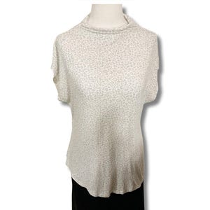 Könnte beinhalten: Ein weißes, kurzärmeliges Shirt mit einem hellgrauen Tiermuster. Das Shirt hat einen Stehkragen und einen leicht abgerundeten Saum.