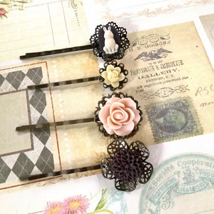 Op de afbeelding: Vier haarclips met decoratieve bloem- en dierenaccenten. De clips zijn gemaakt van metaal met een donkerbruine afwerking. De bloemaccenten zijn gemaakt van wit, roze en bruin hars. Het dierenaccent is een wit konijn. De clips zijn gerangschikt op een gepatroneerde achtergrond.