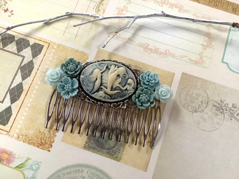 May include: A silver hair comb with a cameo featuring a white porcelain design of three mermaids. The comb is decorated with blue and green flower accents.