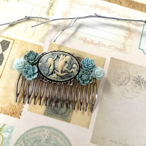 May include: A silver hair comb with a cameo featuring a white and blue mermaid design. The comb is decorated with light blue and white flowers.
