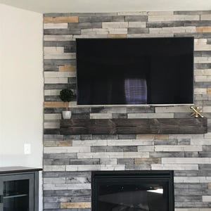 May include: A modern fireplace with a black mantel and a black fireplace insert. The fireplace is surrounded by a gray and white stone wall.