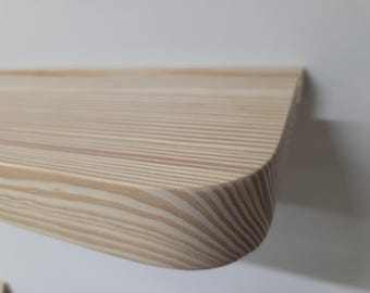 May include: A light-colored wooden shelf with a smooth, rounded corner edge. The surface displays a prominent, linear wood grain pattern in shades of tan and cream, showing the natural texture and horizontal lines of the wood material.