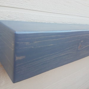May include: A light blue wooden shelf with a rustic, distressed finish. The shelf is made of solid wood and has a natural grain pattern. It is perfect for adding a touch of farmhouse style to any room.