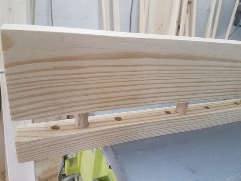 May include: Close-up of a wooden shelf with dowel pins and holes for assembly. The shelf is made of unfinished pine wood.