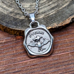 May include: Silver necklace with a pendant featuring a cartoon pterodactyl with the word "PTERRI" inscribed around it.
