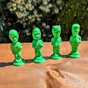 Puede incluir: Cuatro figuras verdes de monstruos, cada una con un diseño único, sobre una superficie de madera. Las figuras incluyen una momia, una criatura de la laguna negra, un hombre lobo y el monstruo de Frankenstein. Las figuras miden unos 7.6 cm de alto.