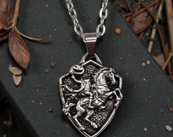 May include: Silver-toned pendant necklace featuring a detailed depiction of the Headless Horseman riding a horse. The pendant is shield-shaped with a textured background and hangs from a linked chain.