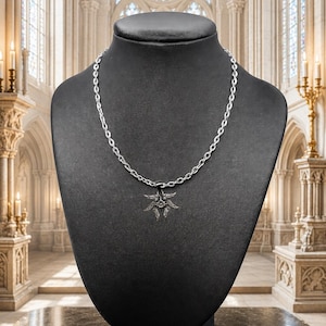 May include: A silver-toned necklace with a sunburst pendant displayed on a black mannequin. The pendant has a detailed, spiky design. The chain is a simple link style. The background is a church interior with stained glass windows and ornate architecture.