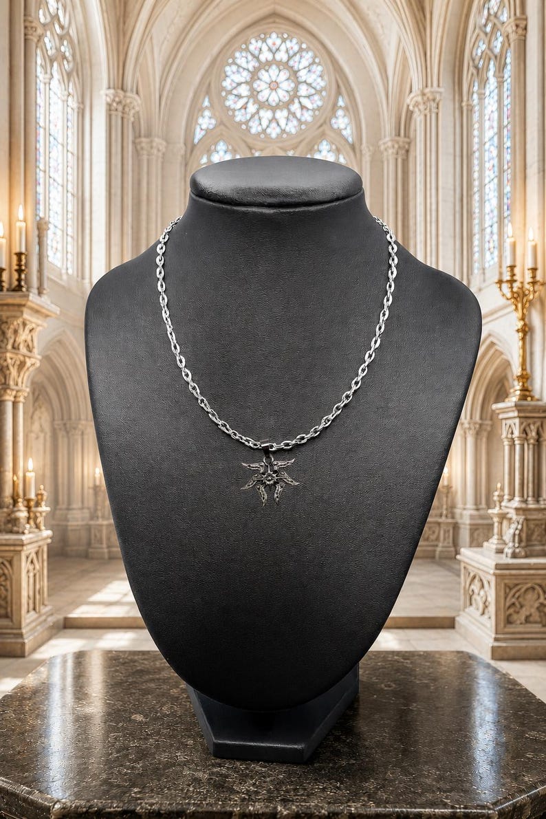 May include: A silver-toned necklace with a sunburst pendant displayed on a black mannequin. The pendant has a detailed, spiky design. The chain is a simple link style. The background is a church interior with stained glass windows and ornate architecture.