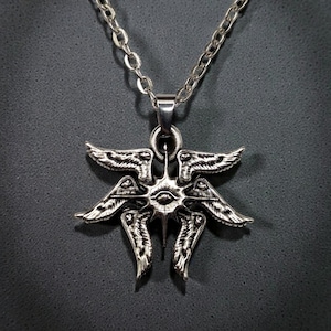 May include: Silver-toned pendant necklace featuring a detailed, stylized design of wings and an eye. The pendant hangs from a delicate chain. The intricate design is visible against a dark background.