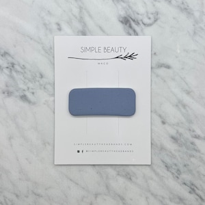 May include: A light blue rectangular hair clip with a speckled texture. The clip is on a white card with the text "SIMPLE BEAUTY WACO SIMPLEBEAUTYHEADBANDS.COM @SIMPLEBEAUTYHEADBANDS"