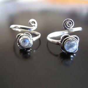 May include: Two silver rings with a moonstone set in a flower design. The rings are open and can be adjusted to fit different finger sizes.