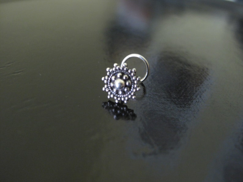 May include: A silver nose ring with a circular design featuring a central bead surrounded by smaller beads.