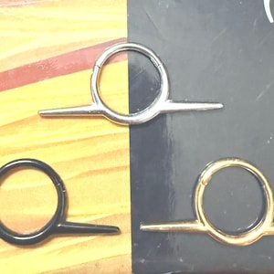 May include: Three metal ring tools with a circular design and two straight extensions. One is silver, one is black, and one is gold. The tools are displayed against a yellow and black background.