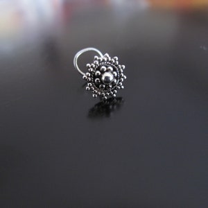 May include: A silver nose ring with a circular design featuring a central bead surrounded by smaller beads.