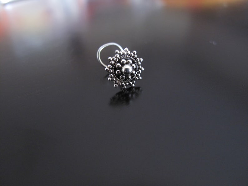 May include: A silver nose ring with a circular design featuring a central bead surrounded by smaller beads.