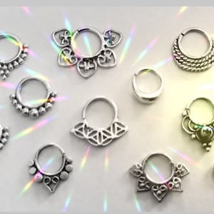Può includere: Una collezione di 12 anelli per il naso in argento con vari disegni decorativi, tra cui motivi floreali, geometrici e perlati.