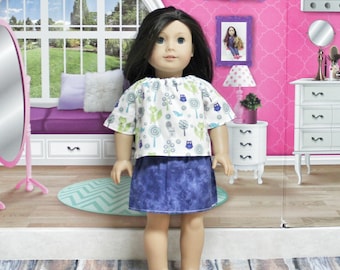 Puede incluir: Una muñeca con una camisa de estampado blanco y azul con búhos y bastones de caramelo y una falda vaquera azul.