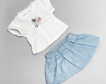 Puede incluir: Una camiseta blanca con un diseño de bordado floral y una falda azul claro con lunares blancos.