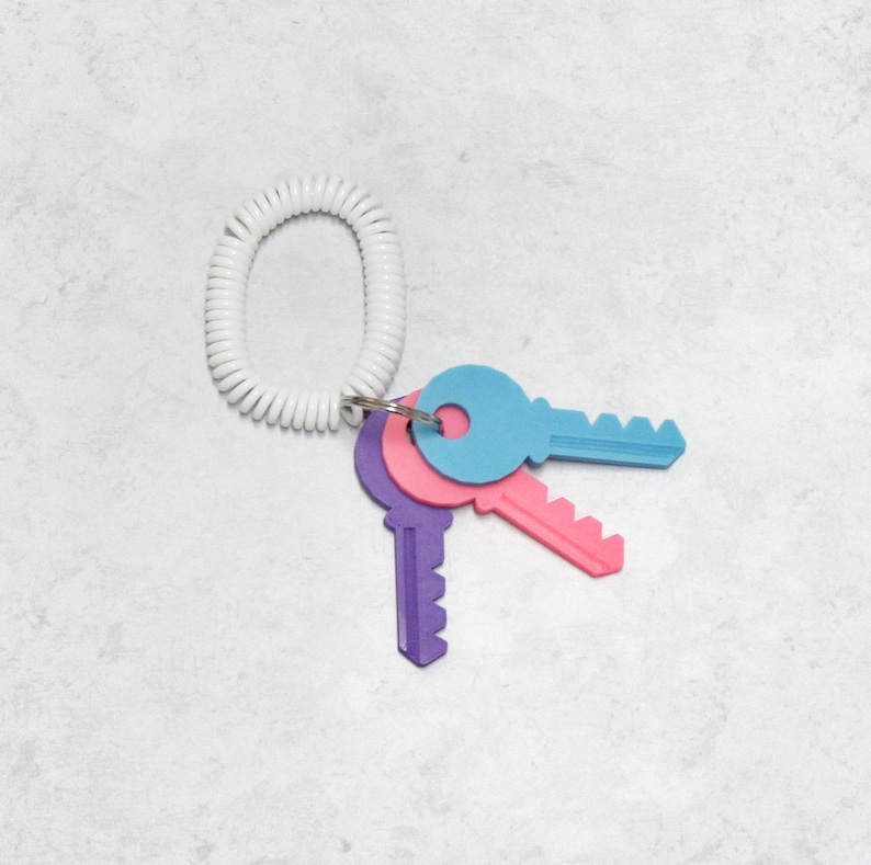 May include: Three plastic keys on a white coiled key chain. The keys are blue, pink, and purple.