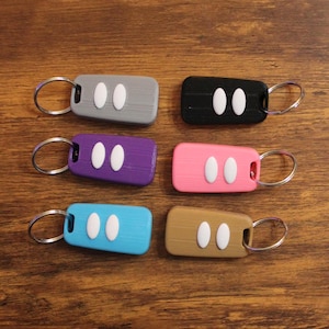 May include: Six keychains with different colored plastic key fob cases. Each keychain has a silver ring and two white buttons. The colors of the key fobs are gray, black, purple, pink, blue, and brown.